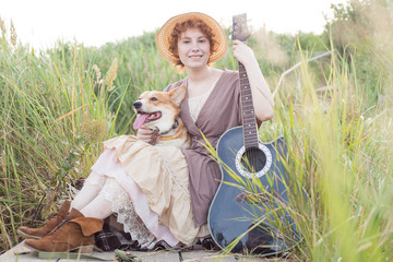 Fototapeta premium redhead woman with guitar and corgi dog in countryside