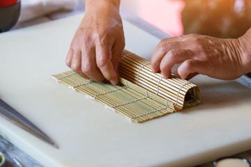 Male hands touch bamboo mat. Small mat on cooking board. Japanese chef at work. Man prepares sushi...