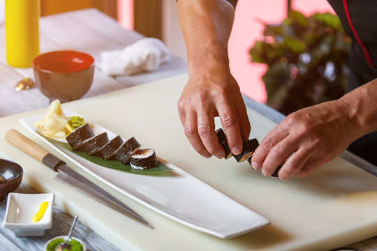Male hands hold sushi rolls. Long white plate with sushi. Best dish from japanese restaurant. Healthy and savoury food.