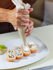 Plate with sushi rolls. Man holds pastry bag. Chef adds fresh cream cheese. Decoration of uramaki rolls.