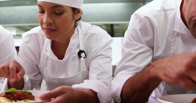 Row of chefs garnishing spaghetti dishes with basil leaf