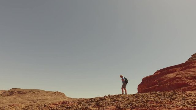 Woman climber conquers the desert and mountains.Girl with a backpack walking along the stone red desert. Steady shot