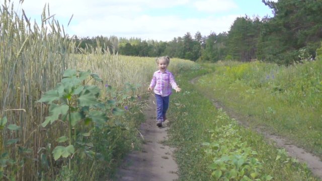  Little girl running on a rural road near the wheat field and smiling. toward the camera . Wide shot.Slow motion.