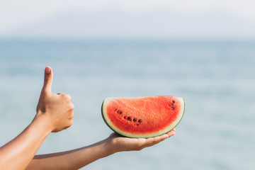 Girl holding a piece of watermelon in hand by the sea