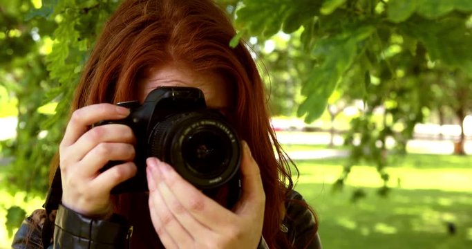 Pretty redhead taking a photo in the park on a sunny day