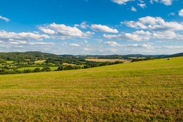 Summer hilly landscape withe green field, forests, blue sky and white clouds, Central Bohemia, Czech Republic