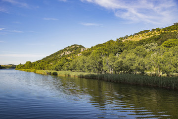 Calm river flowing at the foot of a high rocky hill