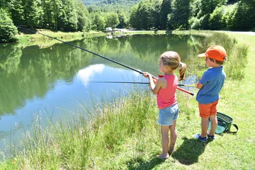 Rolgordijnen Kids fishing by mountain lake in summer © goodluz