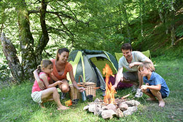 Family camping and cooking sausages in campfire