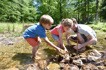 Father and kids in river building a dam with pebbles