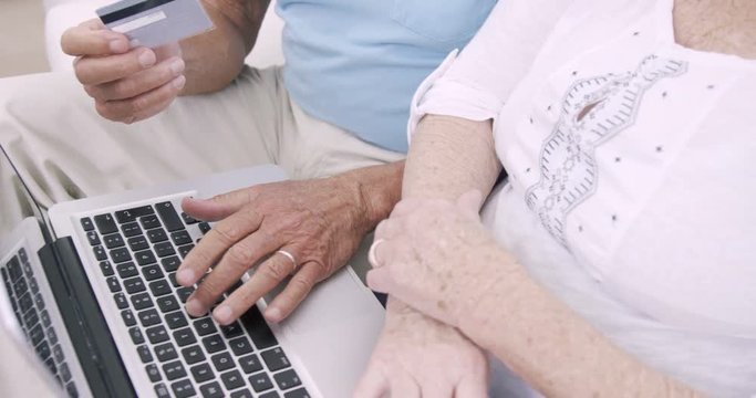 Senior couple using laptop and holding credit card