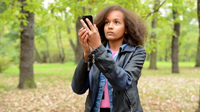 young charming bored african girl make selfie with smartphone in the forest - change pose 
