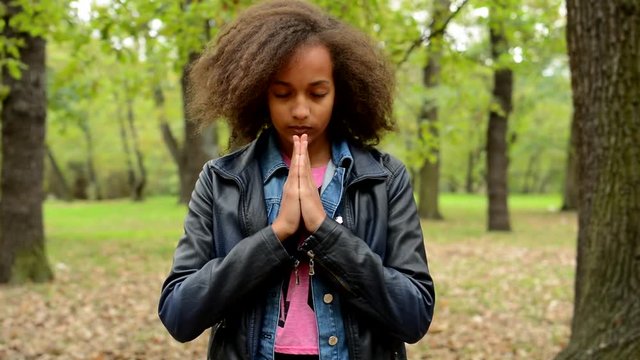 young charming sensitive girl closed eyes and start to pray in the park 