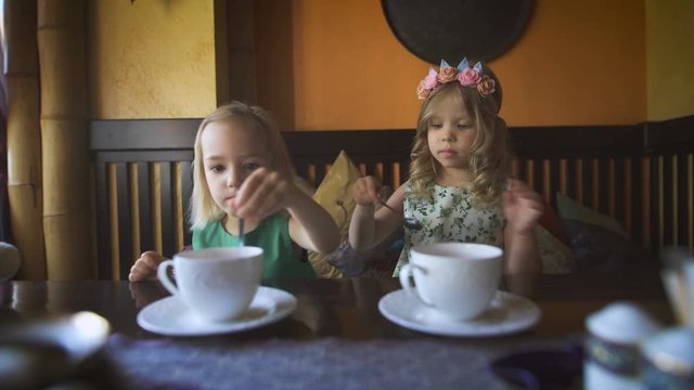 Two cute little girls are having tea in a cafe