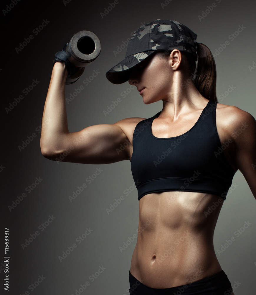 Wall mural strong fitness woman bodybuilder with tanned body pumps up the muscles lifting dumbbells.