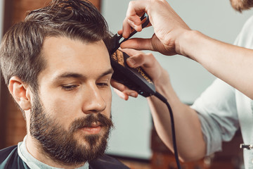 Fototapeta premium The hands of young barber making haircut attractive man in barbershop