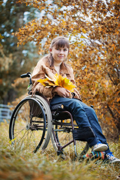 The smiling disabled girl in wheelchair in the autumn park