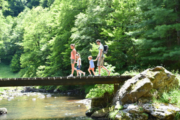 Family of four walking on a bridge crossing the river - obrazy, fototapety, plakaty
