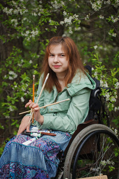 Young woman sitting in a wheelchair , smiling and holding brushe