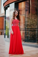 Obraz premium Portrait of fashionable girl at red evening dress posed background mirror window of modern building