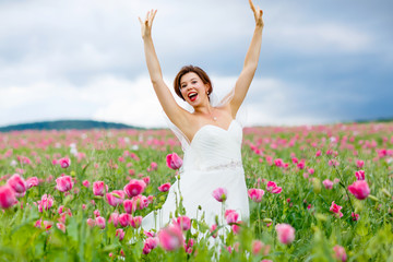 Fototapeta na wymiar happy bride in white dress having fun in flower poppy field 