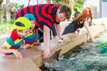 Teacher and two little kid boys feeding rays in a recreation are