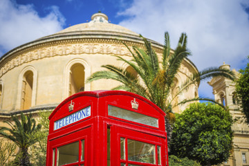 Malta - Traditional British red telephone box with palm trees and the famous Mosta Dome at background
