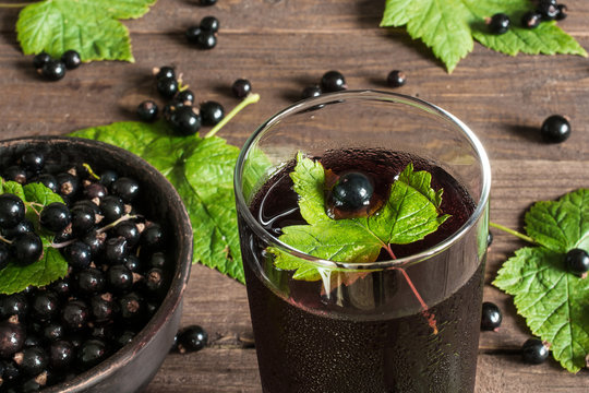 glass of cold black currant juice on wooden table with ripe berr