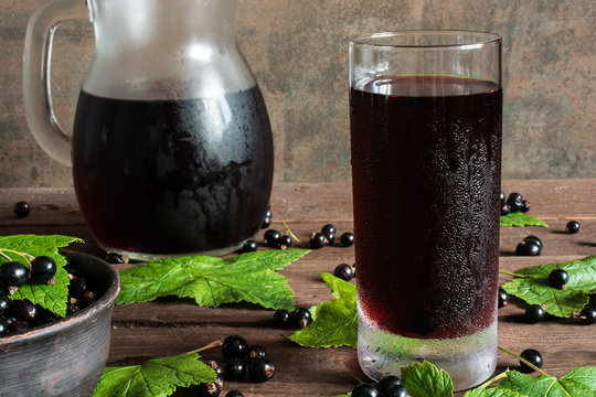 cold black currant juice in a glass and pitcher on wooden table