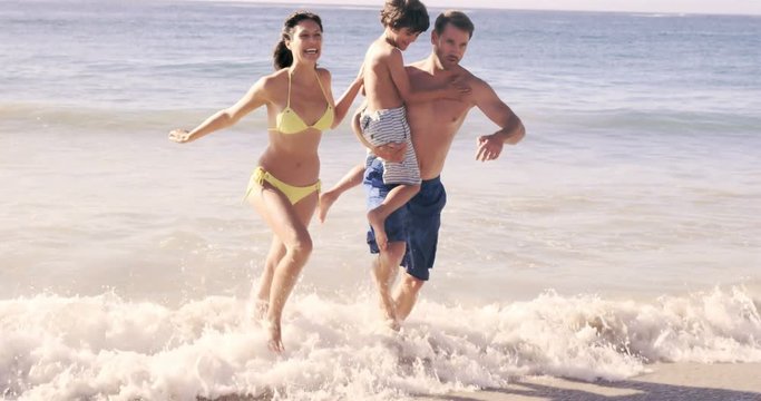 Cute family running out of the water on the beach in slow motion