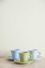 Pile of colorful coffee cups on wooden table with cream background. Top space of frame, wallpaper.