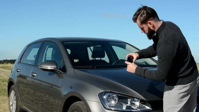 young smart punctual handsome man take a picture of his car with smartphone in the countryside