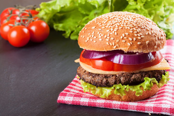Homemade cheeseburger on black slate surface.