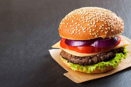 Homemade cheeseburger on black slate surface.