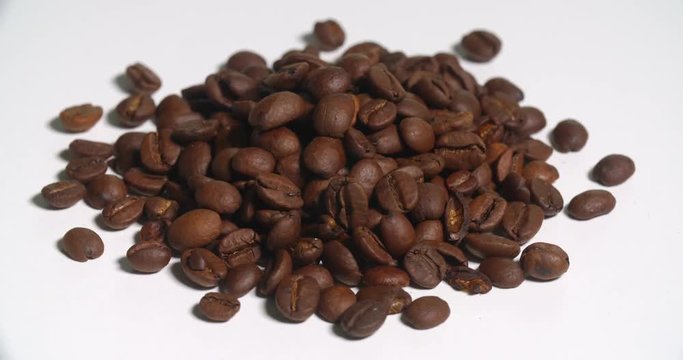 Coffee Beans Pile Uncooked Spinning on White. a pile of brown coffee beans spins left on white
