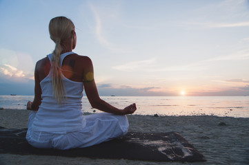 Fototapeta na wymiar Young woman meditating at the beach at sunset