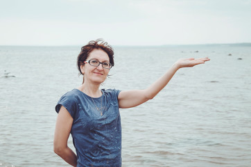 Beauty portrait of attractive mature healthy woman enjoying happy, show shell on her hand. Smiling female standing  seaside with grey cloudy sky, blue baltic sea views, outdoors. Nature background