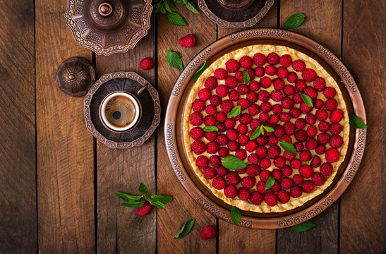 Tart with raspberries and whipped cream decorated with mint leaves on a wooden background. Top view