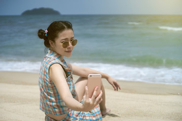 young asian woman take a selfie by smartphone on the beach with blurred sea background,selective focus,filtered image,light effect added