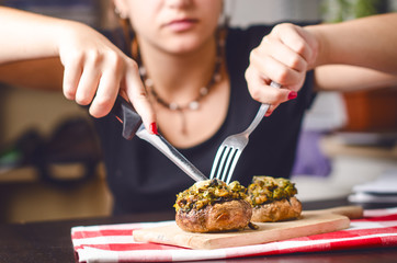 Female hands holding knife and fork and cutting meal. Mushrooms with cheese on a tablecloth. Appetizer. Food background