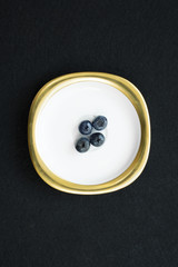 Group of bilberries placed on a golden dish with black isolated background
