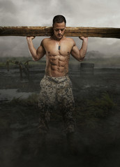 Shirtless male with wooden timber in a swampland.