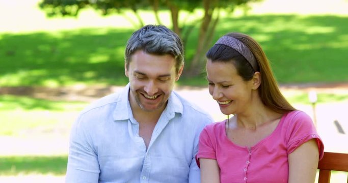 Happy couple sitting on a park bench using tablet pc