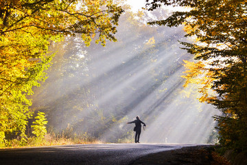 Man with arms open towards morning sunlight rays - obrazy, fototapety, plakaty