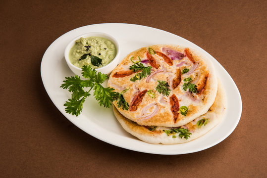 south indian food, two uttapam with coconut chutney in white ceramic plate with coriander leaf, closeup