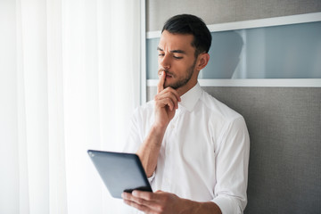 Beautiful businessman brunet working, searching, reading  on the device, gadget in the office. Business.Thinking with hand in the mouth.t