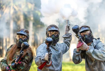 Tuinposter Three paintball players with guns and smoke grenade aiming © Vanoa2