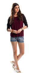 Lady in long sleeve top. Sandals and blue denim shorts. Red top with black sleeves. Model wears stylish summer outfit.