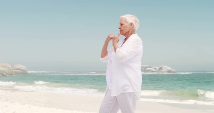 Old retired woman doing some yoga on the beach