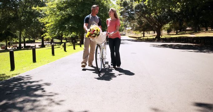 Happy couple walking with bike and bunch of flowers on a sunny day